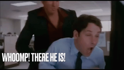 A Man In A Suit And Tie Is Yawning While A Woman Stands Behind Him And Says Whoomp There He Is ! GIF