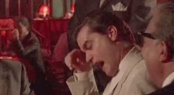A Man In A Suit And Tie Is Yawning While Sitting At A Table In A Bar . GIF