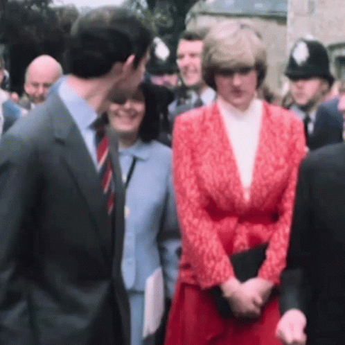 A Man In A Suit And Tie Kisses A Woman In A Red Jacket . GIF