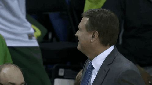 A Man In A Suit And Tie Laughs While Sitting In The Stands GIF