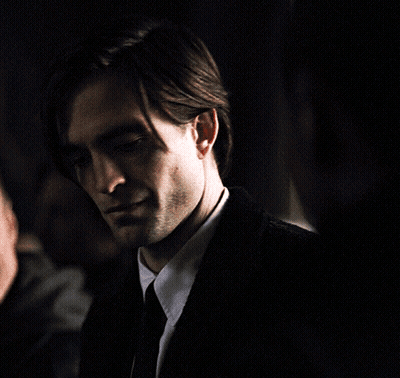 A Man In A Suit And Tie Looks At The Camera In A Dark Room GIF