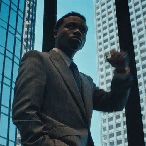 A Man In A Suit And Tie Looks Out A Window GIF