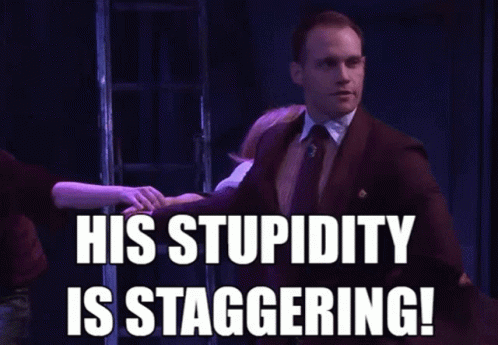 A Man In A Suit And Tie Says His Stupidity Is Staggering In Front Of A Group Of People GIF