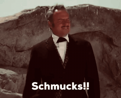A Man In A Suit And Tie Says Schmucks In Front Of A Rock GIF