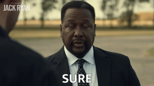 A Man In A Suit And Tie Says Sure In Front Of A Sign That Says Jack Ryan GIF