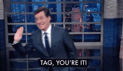 A Man In A Suit And Tie Says Tag You 'Re It In Front Of A Window GIF