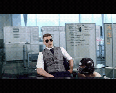 A Man In A Suit And Tie Sits At A Desk In Front Of A White Board That Says ' A ' On It GIF