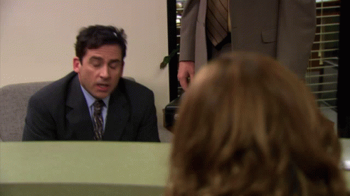 A Man In A Suit And Tie Sits At A Desk In Front Of A Woman GIF