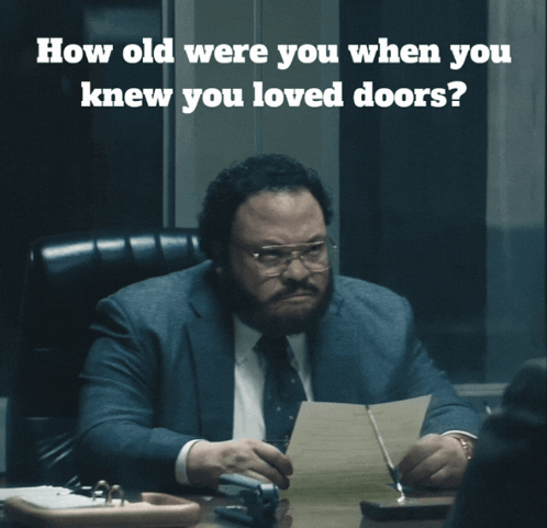 A Man In A Suit And Tie Sits At A Desk With A Question About How Old He Was When He Knew You Loved Doors GIF
