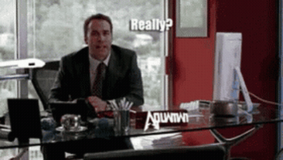 A Man In A Suit And Tie Sits At A Desk With A Sign On It That Says ' Really ? ' GIF
