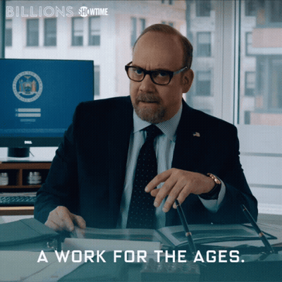 A Man In A Suit And Tie Sits At A Desk With The Words " A Work For The Ages " Above Him GIF