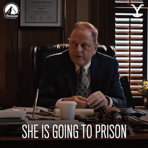 A Man In A Suit And Tie Sits At A Desk With The Words She Is Going To Prison Written Below Him GIF
