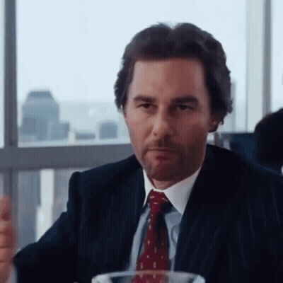 A Man In A Suit And Tie Sits At A Table GIF