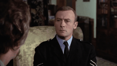 A Man In A Suit And Tie Sits In A Chair GIF