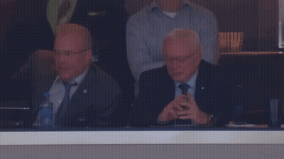 A Man In A Suit And Tie Sits In A Stadium Watching A Game GIF