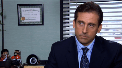A Man In A Suit And Tie Sits In Front Of A Framed Certificate Of Authentication GIF