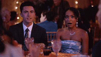 A Man In A Suit And Tie Sits Next To A Woman In A Strapless Blue Dress GIF