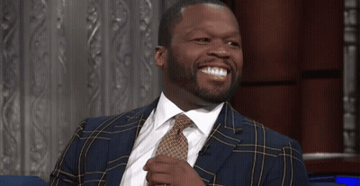 A Man In A Suit And Tie Sits On A Blue Couch GIF