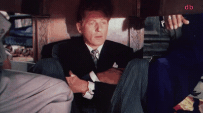 A Man In A Suit And Tie Sits Under A Table With The Letters Db In The Corner GIF