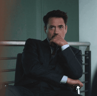 A Man In A Suit And Tie Sits With His Hand On His Chin GIF