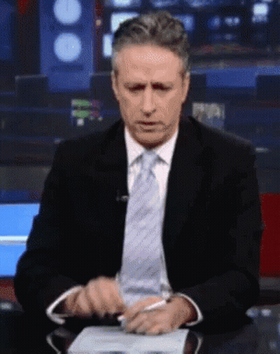 A Man In A Suit And Tie Sitting At A Desk GIF