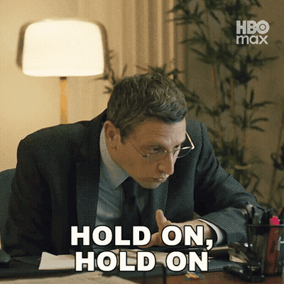 A Man In A Suit And Tie Sitting At A Desk With The Words Hold On Hold On GIF