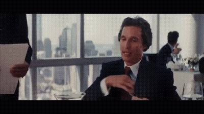 A Man In A Suit And Tie Sitting At A Table GIF