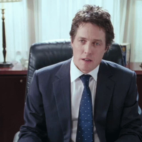 A Man In A Suit And Tie Sitting In A Chair GIF