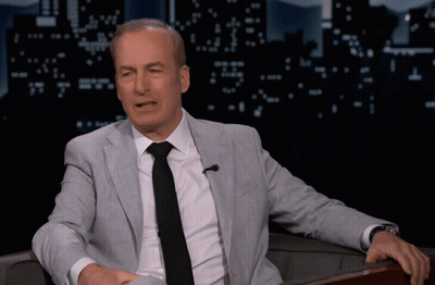 A Man In A Suit And Tie Sitting In A Chair GIF