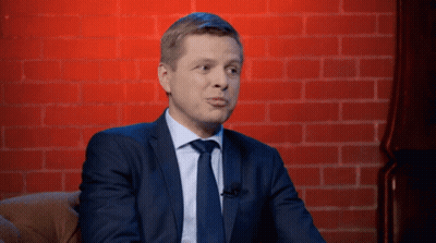 A Man In A Suit And Tie Sitting In Front Of A Brick Wall GIF