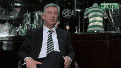 A Man In A Suit And Tie Sitting In Front Of A Celtic Tv Sign GIF