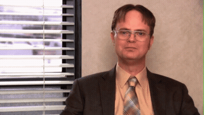 A Man In A Suit And Tie Sitting In Front Of A Window With Blinds GIF