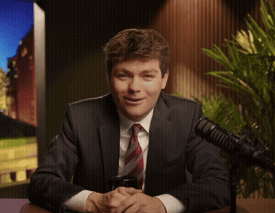 A Man In A Suit And Tie Smiles In Front Of A Microphone GIF