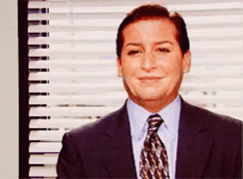 A Man In A Suit And Tie Smiles In Front Of A Window With Blinds GIF