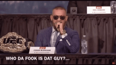 A Man In A Suit And Tie Speaking Into A Microphone With A Sign That Says Conor Mcgregor On It GIF