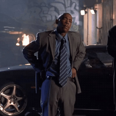 A Man In A Suit And Tie Standing In Front Of A Car GIF