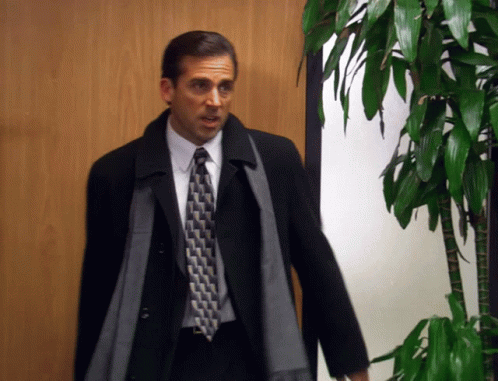 A Man In A Suit And Tie Standing In Front Of A Plant GIF