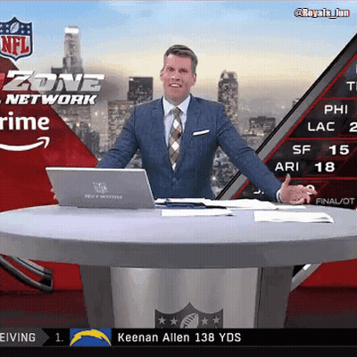 A Man In A Suit And Tie Stands At A Table With A Laptop In Front Of A Screen That Says Zone Network GIF