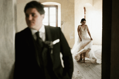 A Man In A Suit And Tie Stands Behind A Bride In A Wedding Dress GIF