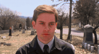 A Man In A Suit And Tie Stands In A Cemetery Looking At The Camera GIF