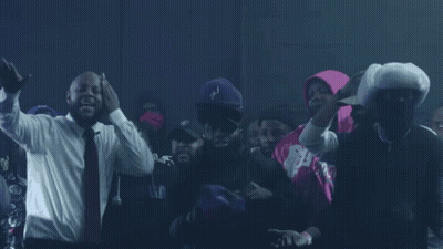 A Man In A Suit And Tie Stands In A Crowd GIF