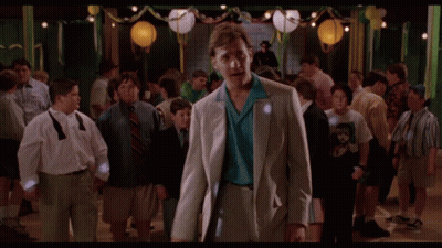 A Man In A Suit And Tie Stands In A Crowd Of People At A Party GIF
