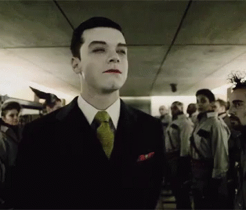 A Man In A Suit And Tie Stands In A Crowd Of People GIF
