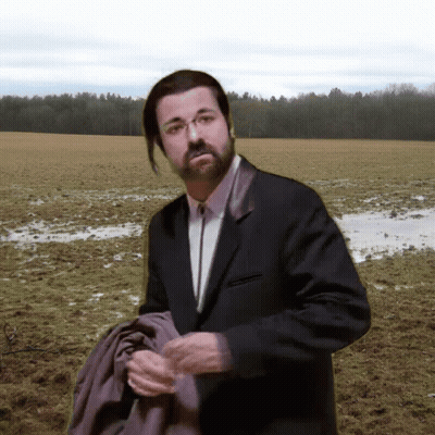 A Man In A Suit And Tie Stands In A Field GIF