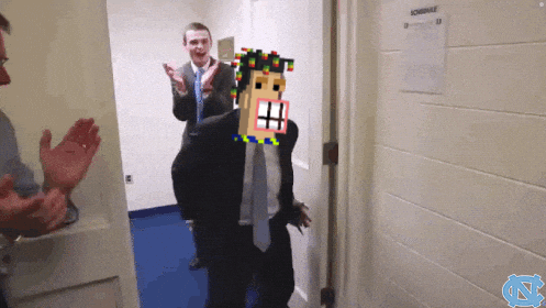 A Man In A Suit And Tie Stands In A Hallway With A Schedule On The Wall Behind Him GIF