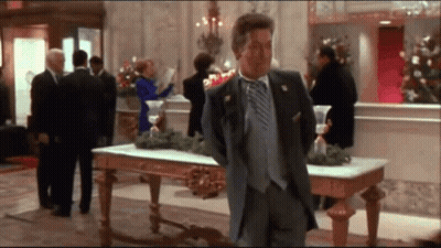 A Man In A Suit And Tie Stands In A Lobby GIF