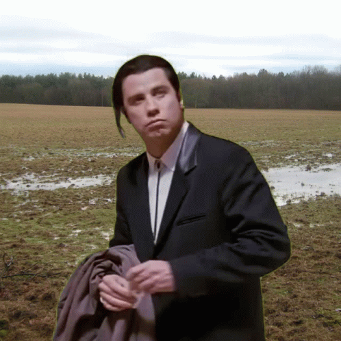 A Man In A Suit And Tie Stands In A Muddy Field GIF