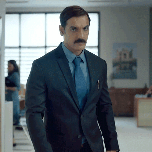 A Man In A Suit And Tie Stands In An Office GIF
