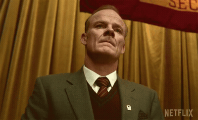 A Man In A Suit And Tie Stands In Front Of A Banner That Says Netflix GIF
