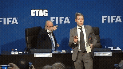 A Man In A Suit And Tie Stands In Front Of A Blue Wall That Says Fifa GIF